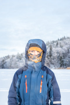 Arctic outdoor winter portrait of a child boy in winter clothing with balaclava against frozen landscape background.