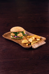 Delicious shrimp burger garnished with potato wedges fried on a wooden board
