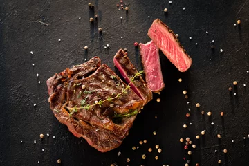 Tuinposter Restaurant cooking art. Grilled steak sliced on textured black background. © golubovy
