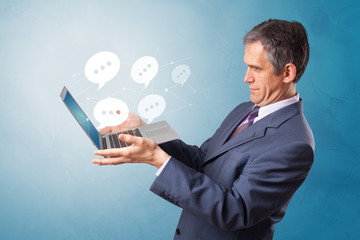Man holding laptop with a few speech bubble symbols
