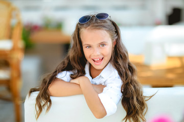 Two cute little girls standing in jumpers and sun glasses on the terrace background in the studio. Summer, fun, family and vacations concept. Two fashion sisters posing.