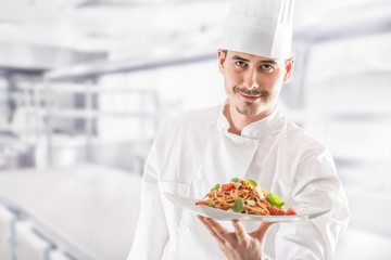 Chef in restaurant kitchen holding plate with italian meal spagh