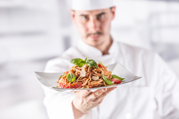 Chef in restaurant kitchen holding plate with italian meal spaghetti bolognese