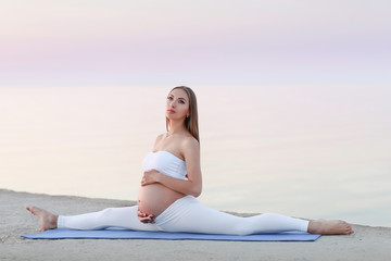 Fototapeta na wymiar Beautiful pregnant woman doing yoga at the sea side