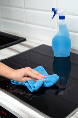 A woman's hand with a blue microfiber cloth rubs a glass ceramic plate in the kitchen. In the...
