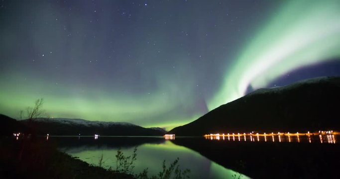northern lights time lapse reflecting in the water of a Fjord in Norway in green blue and violette colours 