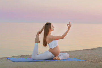 Fototapeta na wymiar Young pregnant woman in white dress sitting on the beach near blue sea and breathing. Summer vacation during pregnancy, happy motherhood concept, close up on hands
