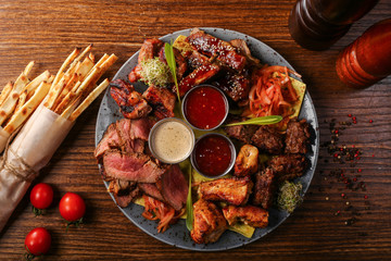 dish of different cook meat with sous and tomato on black wood background 