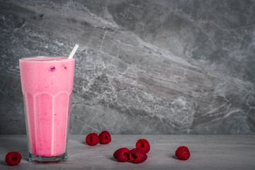 A glass of dairy free milkshake with fresh organic raspberries on a marble stone background with copy space