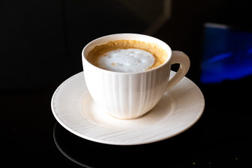 White cup of coffee, saucer on a black background.