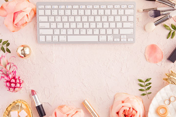 Top view of woman beauty blogger working desk with computer keyboard and laptop, decorative cosmetic, flowers and palm leaves, envelope on pink pastel table. Flat lay background