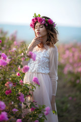 Naklejka premium Young beautiful girl in a long dress and a wreath of flowers in the garden of lilac bush