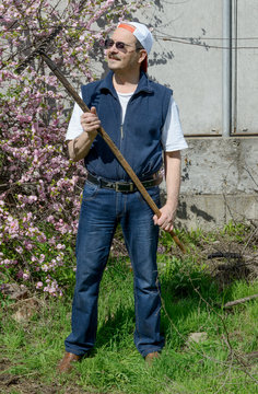 Man is standing with rake near flowering Prunus triloba bush.
