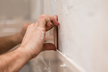 Stylish trendy beige ceramic tiles with chamfer on the kitchen wall. Hands tiler in the process of laying white rectangular tiles on the bathroom wall. Repair of apartments and bathrooms.ceramic tile