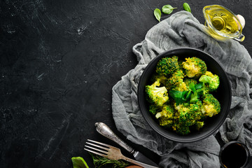 Boiled broccoli in a black plate. On a black background. Top view. Free space for your text.