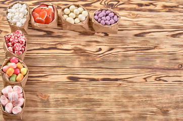 candies, lollipops, caramel, in paper bags on wooden background