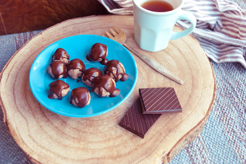 Still Life with homemade healthy candies of nuts and glazed by dark chocolate on blue plate and tea. Vegan dessert background.