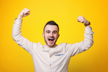 Naklejka premium Portrait of a satisfied young man celebrating success with haraised hands over yellow background