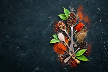 Fototapeten Pepper in a spoon. Colored pepper, sea salt, ground pepper, chili pepper. Top view. On a black background. © Yaruniv-Studio