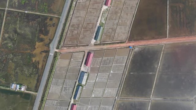 Aerial view high above geometric pattern of salt evaporation fields in Asia; large salt storage structures and some roads can be seen nearby.