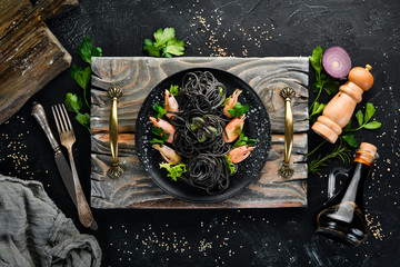 Black pasta with shrimps on a black plate. Top view. On a black background. Free copy space.