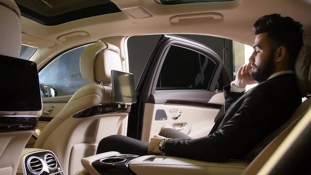 Young male businessman talking on the phone in a luxury car