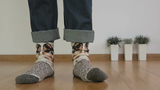Close-up of the legs of a man in warm wool socks are standing on the wooden floor in the room and trampling