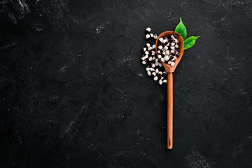 Raw beans in a wooden spoon on a black background. Top view. Free copy space.