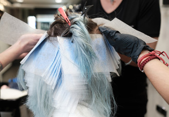 Una mujer recibe el tinte en una peluquería y se ven las manos de la peluquera
