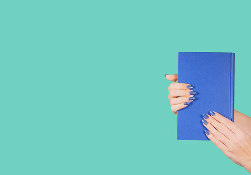 Closeup view of two female hands holding blue paper book isolated on green background with copyspace. Horizontal color photography,