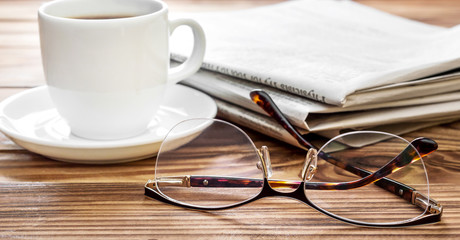 Eyeglasses with newspapers and cup of coffee on the table.