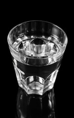 Glass of water on black reflective background.