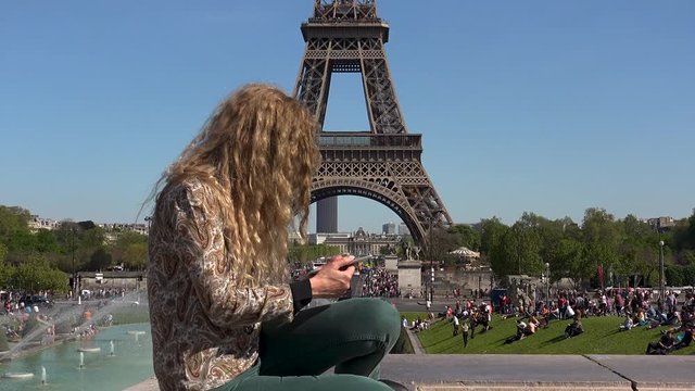 Beautiful woman with hair in the wind captures moments and memories near the Eiffel Tower
