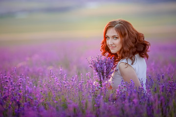 Fototapeta na wymiar Redhead young woman in brightly summer dress looking out onto the fields of lavender on the plateau of Valensole, France.