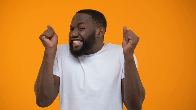 Young Afro-American man extremely happy, lottery winner, yellow background