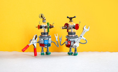 Maintenance repair service concept. Two comical electrician robots are ready for maintenance. Robotic toy handymans red pliers hand wrench on yellow gray background.