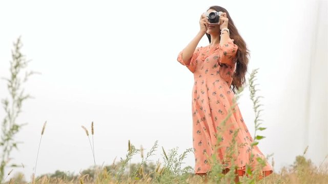 Very beautiful girl with a camera in hand. Photographs peyzh. Slow motion. Field with green grass