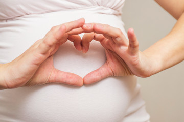 Woman holding her hands in a heart shape on her pregnant belly. Pregnant Belly with fingers Heart symbol. Maternity concept