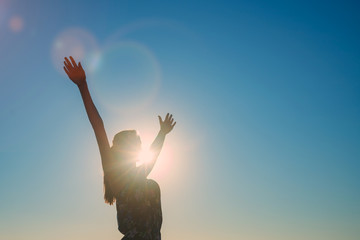 Silhouette of a girl with arms wide apart, blue sky background, bright sun and rays