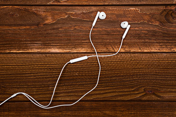 Headphones resting on table top. Headphones with white cable. Modern device for listening music. Sound earphones lying on wooden rustic background