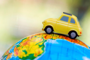 A car on globe on green background. Miniature car toy on globe. Travel concept