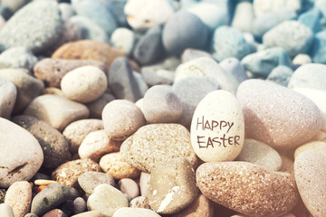 Easter egg from a stone with the inscription Happy Easter on the sea pebble beach, toned. Easter background
