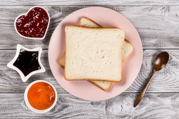 Delicious toasts on pink plate with sweet jams and wooded spoon on wooden background