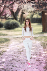 Outdoor portrait of young beautiful happy smiling lady posing near flowering tree. Model wearing stylish accessories clothes. Girl closed her eyes. Female beauty fashion concept. City lifestyle.