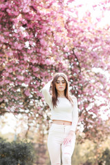 Outdoor portrait of young beautiful happy smiling lady posing near flowering tree. Model wearing stylish accessories clothes. Girl closed her eyes. Female beauty fashion concept. City lifestyle.