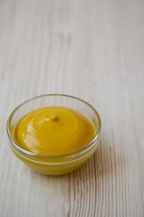 Homemade organic mustard in glass bowl on white wooden background, low angle view. Copy space.