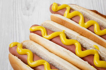 Hot-dog with yellow mustard on wooden board on white wooden background, low angle view. Close-up.