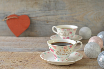 A cup of coffee on a wooden background. A red wooden heart in the background