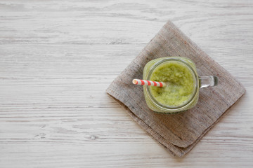 Green celery smoothie in glass jar over white wooden table, overhead view. Flat lay, from above, top view. Copy space.
