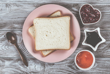 Delicious toasts on pink plate with sweet jams and wooded spoon on wooden background